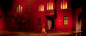 Movie still from “Suspiria” (1977), directed by Dario Argento – A woman sitting in front of a building at night; Extreme Wide shot, Low angle