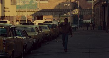 Movie still from “Taxi Driver” (1976), directed by Martin Scorsese – A woman walking down a street past parked cars; Wide shot, Over the shoulder angle