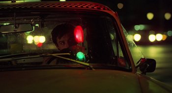 Movie still from “Taxi Driver” (1976), directed by Martin Scorsese – A man sitting in the drivers seat of a taxi cab; Close Up shot, Low angle