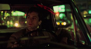 Movie still from “Taxi Driver” (1976), directed by Martin Scorsese – A man sitting in the driver's seat of a car at night; Close Up shot, Low angle