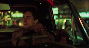 Movie still from “Taxi Driver” (1976), directed by Martin Scorsese – A man sitting in the driver's seat of a car at night; Close Up shot, High angle