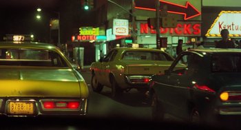 Movie still from “Taxi Driver” (1976), directed by Martin Scorsese – A yellow car is driving down the street at night; Wide shot, Low angle