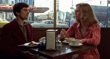 Movie still from “Taxi Driver” (1976), directed by Martin Scorsese – A man and a woman sitting at a table with food on it; Medium shot, Over the shoulder angle