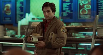 Movie still from “Taxi Driver” (1976), directed by Martin Scorsese – A man holding a plate of food in his hands; Medium shot, Over the shoulder angle