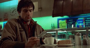 Movie still from “Taxi Driver” (1976), directed by Martin Scorsese – A man sitting in front of a cup of coffee; Medium shot, Low angle