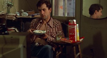 Movie still from “Taxi Driver” (1976), directed by Martin Scorsese – A man sitting at a table with a bowl of cereal; Medium shot, Low angle