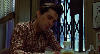 Movie still from “Taxi Driver” (1976), directed by Martin Scorsese – A man sitting at a table looking down at his cell phone; Close Up shot, Low angle