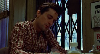 Movie still from “Taxi Driver” (1976), directed by Martin Scorsese – A man sitting at a table with a cigarette in his mouth; Close Up shot, Low angle