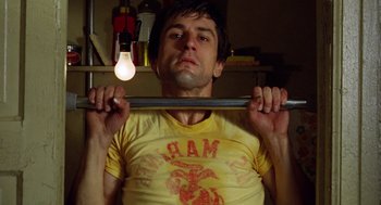 Movie still from “Taxi Driver” (1976), directed by Martin Scorsese – A man holding onto a bar with a light hanging from it; Close Up shot, Low angle