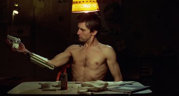 Movie still from “Taxi Driver” (1976), directed by Martin Scorsese – A shirtless man sitting at a table reading a newspaper; Medium shot, Low angle