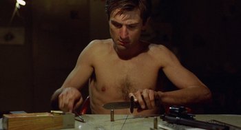 Movie still from “Taxi Driver” (1976), directed by Martin Scorsese – A shirtless man holding a knife in his hand; Medium shot, High angle