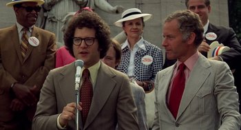 Movie still from “Taxi Driver” (1976), directed by Martin Scorsese – A man in a suit is speaking into a microphone; Medium shot, Over the shoulder angle