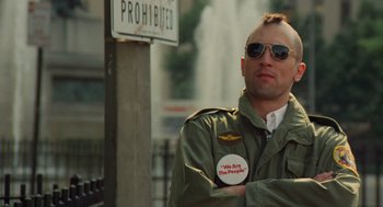 Movie still from “Taxi Driver” (1976), directed by Martin Scorsese – A man wearing sunglasses and an army jacket with a sticker on his chest; Close Up shot, Low angle