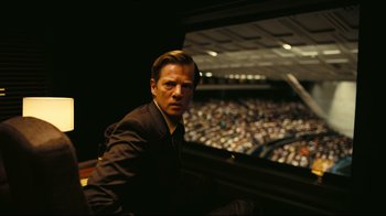 Movie still from “Tenet” (2020), directed by Christopher Nolan – A man sitting in front of an audience in front of an audience hall; Medium shot, High angle