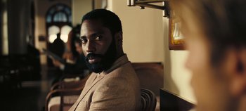 Movie still from “Tenet” (2020), directed by Christopher Nolan – A man with a beard sitting in a chair; Close Up shot, Over the shoulder angle