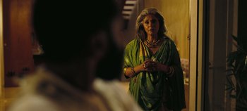 Movie still from “Tenet” (2020), directed by Christopher Nolan – An older woman in a green dress is standing in front of a mirror; Medium shot, Over the shoulder angle