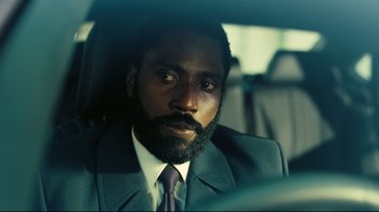 Movie still from “Tenet” (2020), directed by Christopher Nolan – A man in a suit sitting in the back of a car; Close Up shot, Low angle