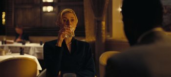 Movie still from “Tenet” (2020), directed by Christopher Nolan – A woman sitting at a table drinking a glass of water; Close Up shot, Over the shoulder angle