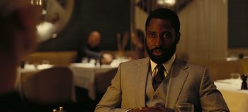 Movie still from “Tenet” (2020), directed by Christopher Nolan – A man wearing a suit and tie in a restaurant; Close Up shot, Over the shoulder angle