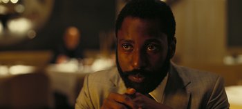 Movie still from “Tenet” (2020), directed by Christopher Nolan – A person wearing a suit and tie; Close Up shot, Over the shoulder angle