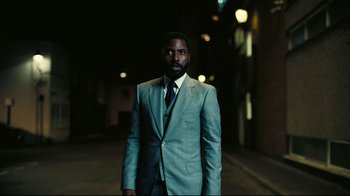 Movie still from “Tenet” (2020), directed by Christopher Nolan – A man in a suit and tie standing in a dark alley; Medium shot, Low angle
