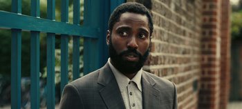 Movie still from “Tenet” (2020), directed by Christopher Nolan – A man in a suit standing in front of a brick wall; Close Up shot, Over the shoulder angle