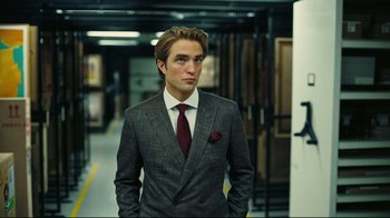 Movie still from “Tenet” (2020), directed by Christopher Nolan – A man in a suit and tie standing in a room; Medium shot, Over the shoulder angle