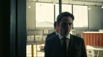 Movie still from “Tenet” (2020), directed by Christopher Nolan – A man in a suit and tie standing in front of a window; Close Up shot, Over the shoulder angle