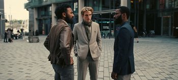 Movie still from “Tenet” (2020), directed by Christopher Nolan – A group of men standing next to each other on a sidewalk; Medium shot, Over the shoulder angle