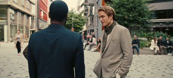 Movie still from “Tenet” (2020), directed by Christopher Nolan – A man in a suit and a tie standing next to another man in a suit and tie; Medium shot, Over the shoulder angle