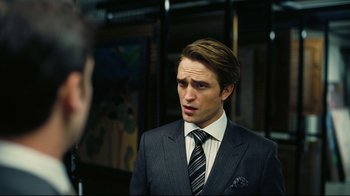 Movie still from “Tenet” (2020), directed by Christopher Nolan – A man wearing a suit and tie talking to someone; Close Up shot, Over the shoulder angle