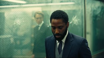 Movie still from “Tenet” (2020), directed by Christopher Nolan – A man wearing a suit and tie standing in front of a glass wall; Medium shot, Over the shoulder angle