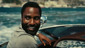 Movie still from “Tenet” (2020), directed by Christopher Nolan – A man smiling while sitting in a boat; Close Up shot, Over the shoulder angle