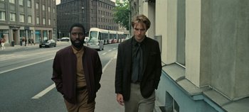 Movie still from “Tenet” (2020), directed by Christopher Nolan – Two men walking down the street in front of a bus; Medium shot, Low angle