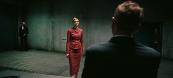 Movie still from “Tenet” (2020), directed by Christopher Nolan – A woman in a red suit standing in front of a man; Medium shot, Over the shoulder angle