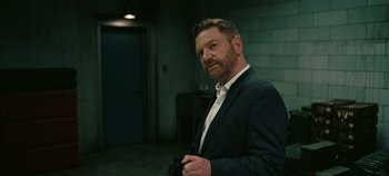 Movie still from “Tenet” (2020), directed by Christopher Nolan – A man in a black suit holding a camera; Medium shot, Over the shoulder angle