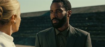 Movie still from “Tenet” (2020), directed by Christopher Nolan – A man with a beard is standing in a suit; Close Up shot, Low angle