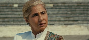 Movie still from “Tenet” (2020), directed by Christopher Nolan – An older woman wearing a white shirt and a colorful scarf; Close Up shot, Over the shoulder angle