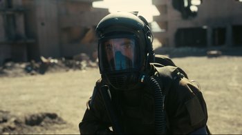 A man wearing a helmet and a gas mask is sitting in the dirt