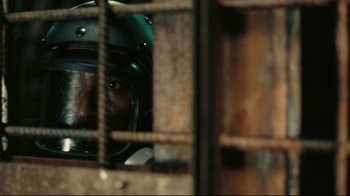 Movie still from “Tenet” (2020), directed by Christopher Nolan – A man wearing a motorcycle helmet looking out of a cage; Close Up shot, Overhead angle