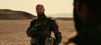 Movie still from “Tenet” (2020), directed by Christopher Nolan – A man with a beard holding a cell phone in his hand; Medium shot, Over the shoulder angle