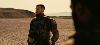 Movie still from “Tenet” (2020), directed by Christopher Nolan – A man with a beard wearing a body armor; Medium shot, Over the shoulder angle
