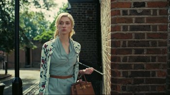Movie still from “Tenet” (2020), directed by Christopher Nolan – A woman holding a brown purse standing next to a brick wall; Medium shot, Low angle