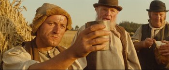Movie still from “Tess” (1979), directed by Roman Polanski – A man holding a cup while standing next to another man in a field; Close Up shot, Low angle