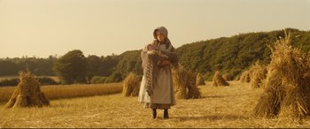 Movie still from “Tess” (1979), directed by Roman Polanski – A woman holding a baby in her arms in a field; Wide shot, Low angle