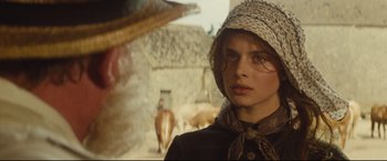 Movie still from “Tess” (1979), directed by Roman Polanski – A young woman in a hat and scarf standing in front of a stone building; Close Up shot, Over the shoulder angle