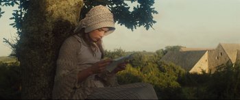 Movie still from “Tess” (1979), directed by Roman Polanski – A woman sitting on a tree branch reading a book; Medium shot, High angle