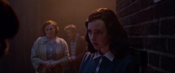 Movie still from “Elvis” (2022), directed by Baz Luhrmann – A woman standing next to a brick wall in front of a group of people; Medium shot, Over the shoulder angle