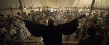 Movie still from “Elvis” (2022), directed by Baz Luhrmann – A group of people standing in a room with their hands up; Medium shot, Low angle