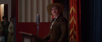 Movie still from “Elvis” (2022), directed by Baz Luhrmann – A man wearing a suit and a hat standing at a podium; Medium shot, Low angle